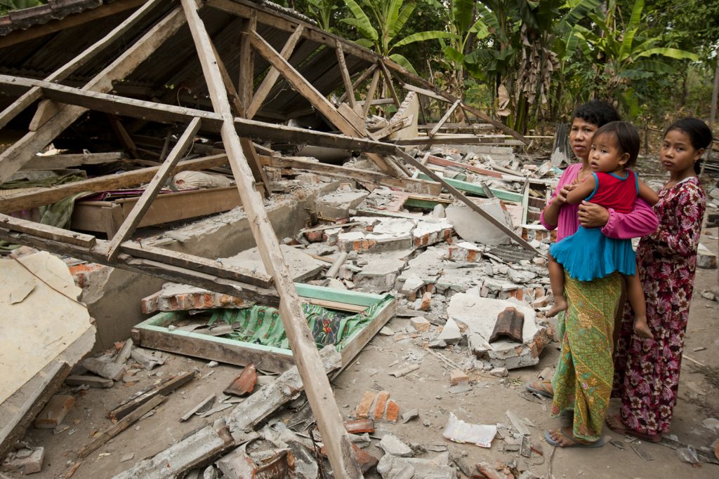 A family stand in front of their collapsed house following an earthquake in Tanjung on August 7, 2018 in Lombok Island, Indonesia